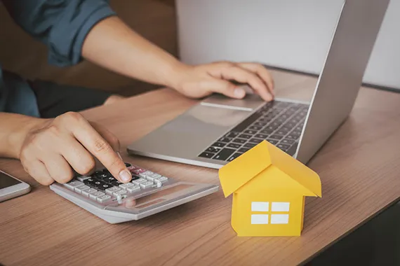Person using a calculator with a house model nearby, symbolizing the advantages of mortgage refinancing.