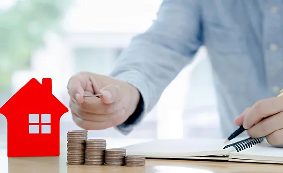 A professional stacking coins next to a small house model, illustrating the advantages of hard money loans for real estate investors.