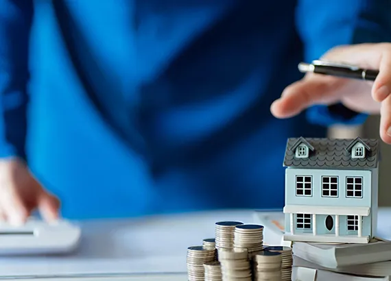 A business professional stacking coins next to a miniature building, highlighting the benefits of fix and flip loans.