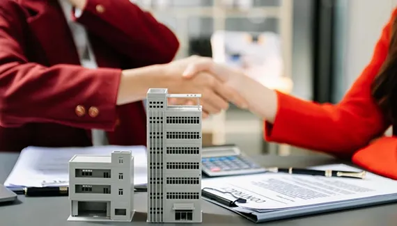 A business meeting with professionals exchanging documents and a model building on the table, depicting commercial short-term loans in Chicago, IL.