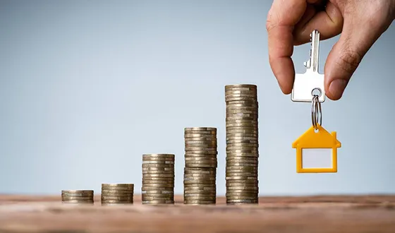 A hand stacking coins with a miniature house in the background, representing mortgage refinancing solutions in Tampa, FL.