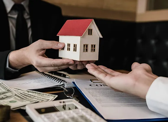Real estate investor presenting a small house model and cash, symbolizing landlord loan services in Las Vegas, NV.