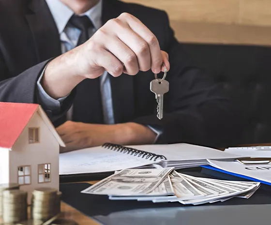 A real estate agent handing over house keys with a small house model and financial documents, symbolizing residential fix and flip loans in Memphis, TN.