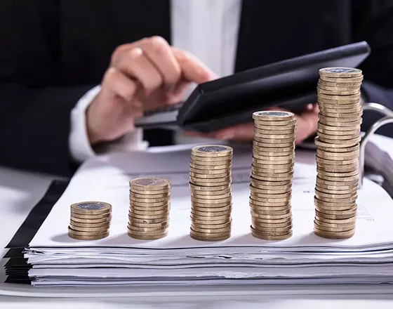A business professional using a magnifying glass to examine stacks of coins, representing financial growth and hard money loan solutions in Las Vegas, NV.