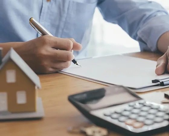 Financial advisor calculating mortgage refinancing options with a small house model on the desk.