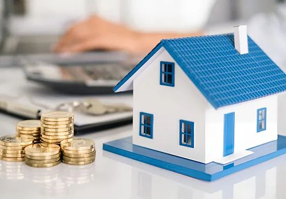 A miniature blue-roofed house next to stacked coins and financial papers, illustrating hard money loans for real estate investment in Las Vegas.