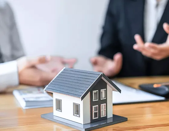 Two professionals discussing real estate financing with a small model house on a desk, representing landlord loan services in Baltimore, MD.