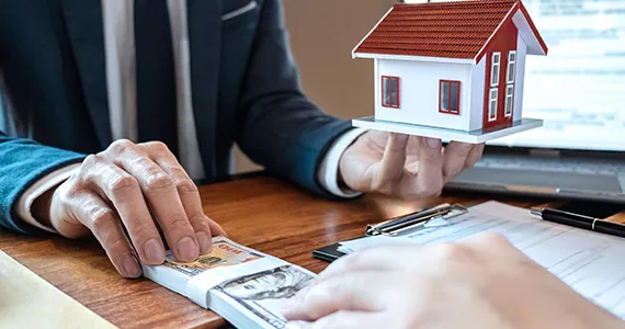A financial advisor presenting mortgage documents with a small house model, representing mortgage refinancing solutions in Baltimore MD.