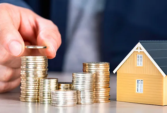 A person stacking coins beside a small house model, symbolizing fix and flip loan services in Baltimore, MD.